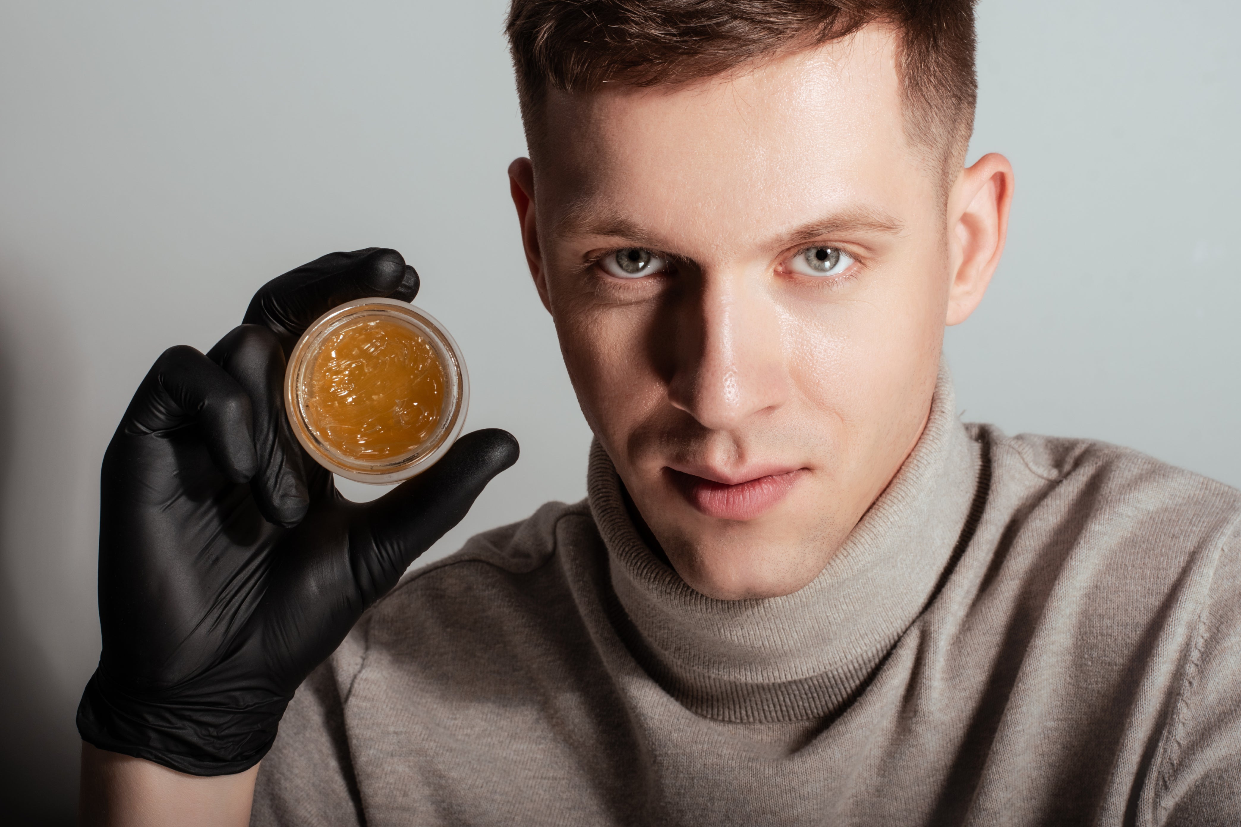 Mees mustas kindas esitleb avatud purki kuldse palsami või geeliga.